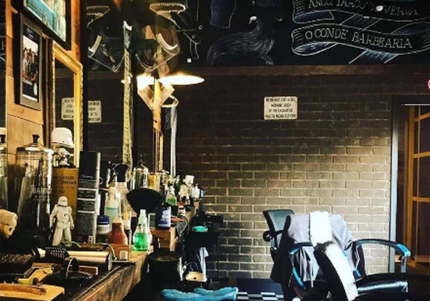 Interior da O Conde Barbearia, com bancada, cadeiras e piso xadrez